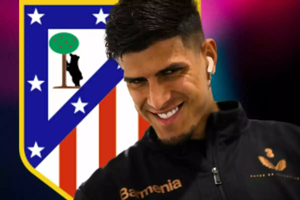 Un futbolista sonriente con auriculares frente al escudo del Atlético de Madrid