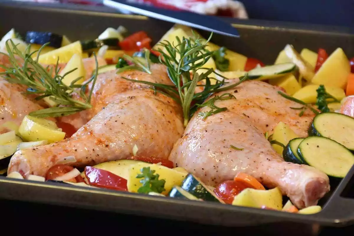 Varios muslos de pollo con verduras y hierbas en una bandeja de horno