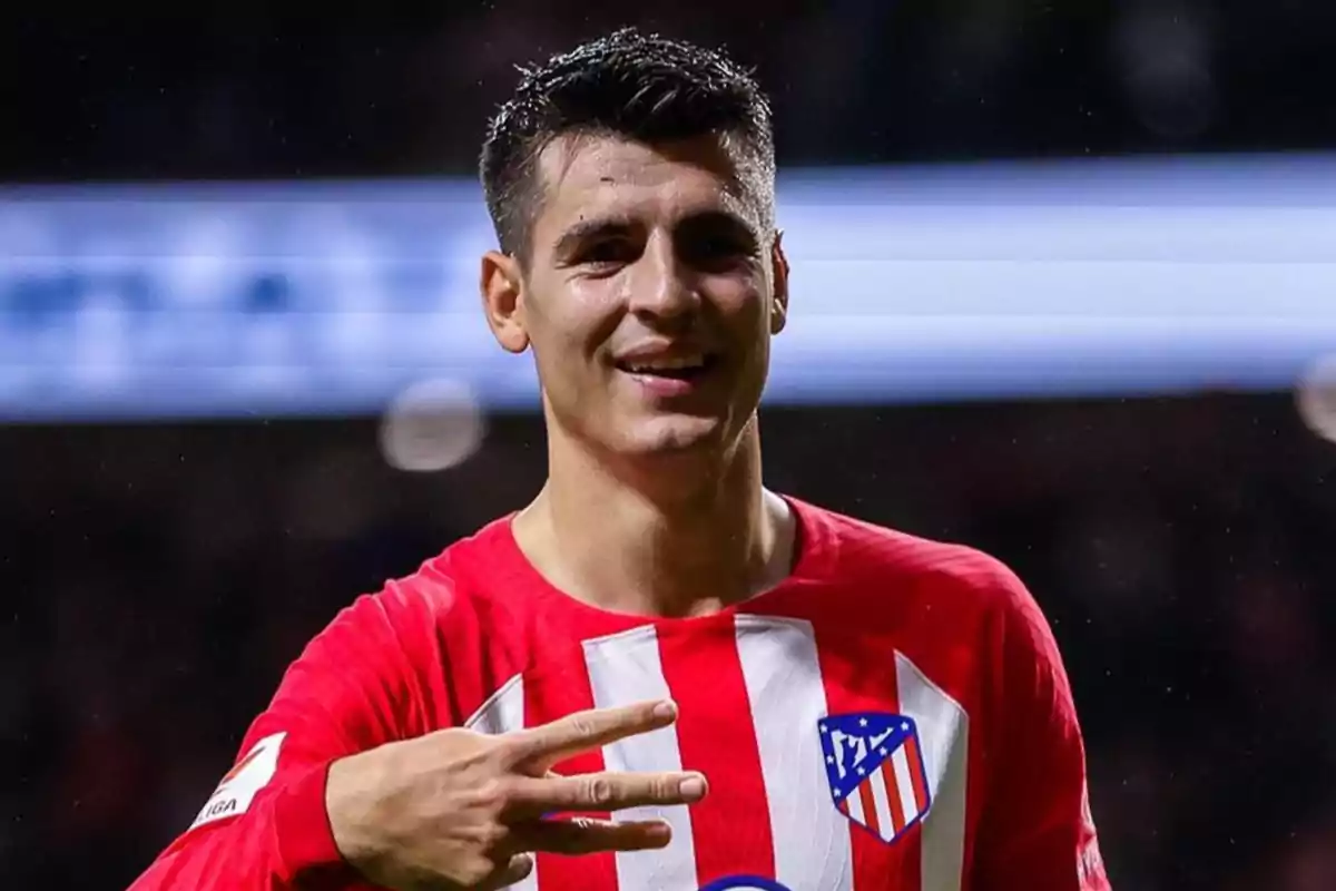 Un jugador de fútbol con la camiseta del Atlético de Madrid sonríe y muestra tres dedos.