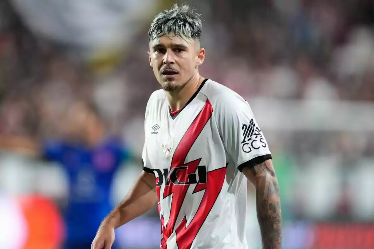 Jugador de fútbol con camiseta blanca y roja en el campo de juego.