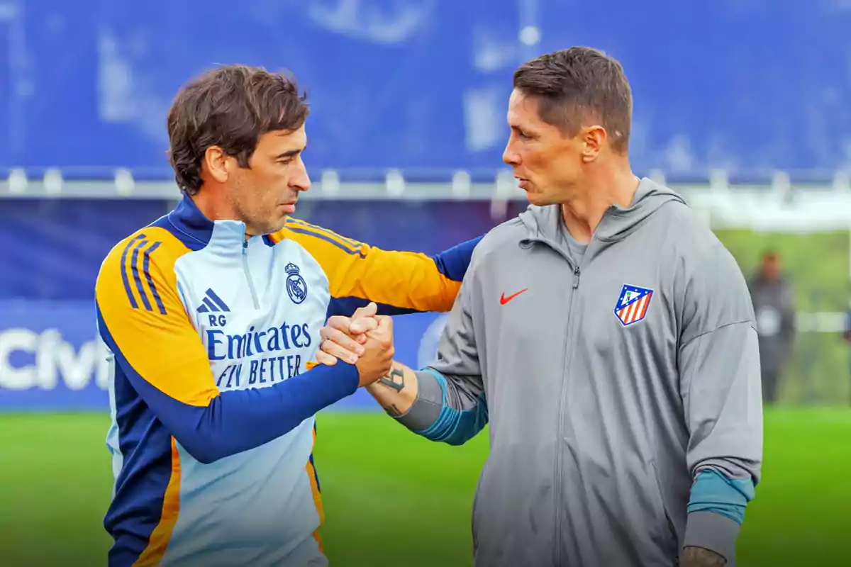 Dos hombres con ropa deportiva de los equipos Real Madrid y Atlético de Madrid se saludan con un apretón de manos en un campo de entrenamiento.