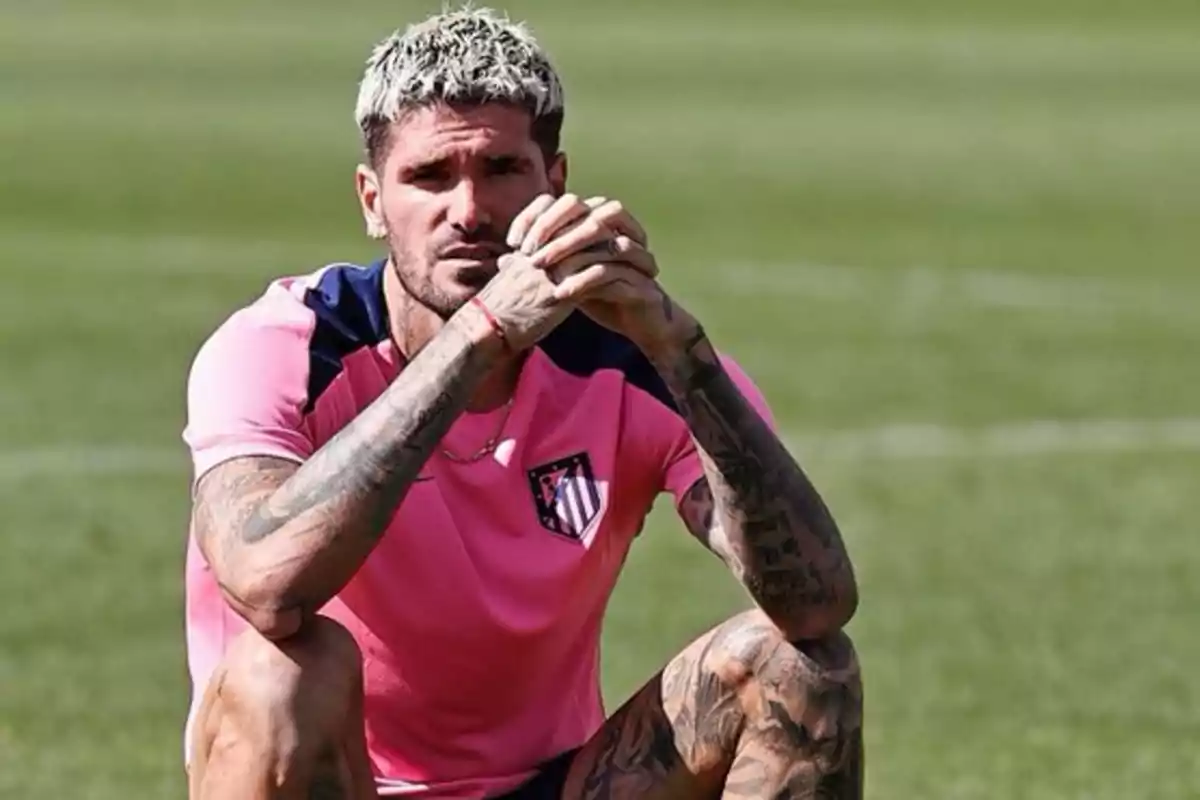 Un jugador de fútbol con uniforme rosa y negro, sentado en el campo de entrenamiento.