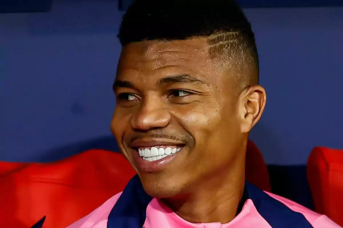 Un hombre sonriendo con una camiseta rosa.