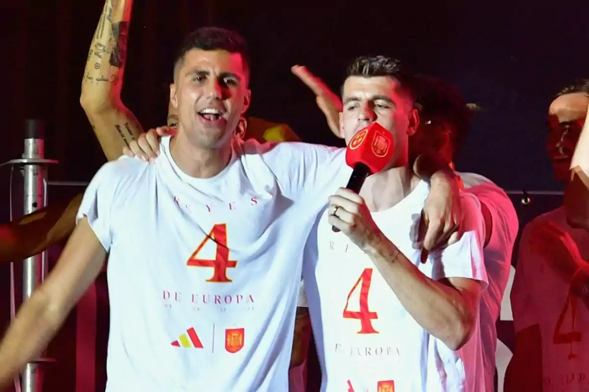 Rodri y Álvaro Morata celebran con camisetas blancas que tienen el número 4 y la frase "Reyes de Europa", Álvaro sostiene un micrófono rojo.