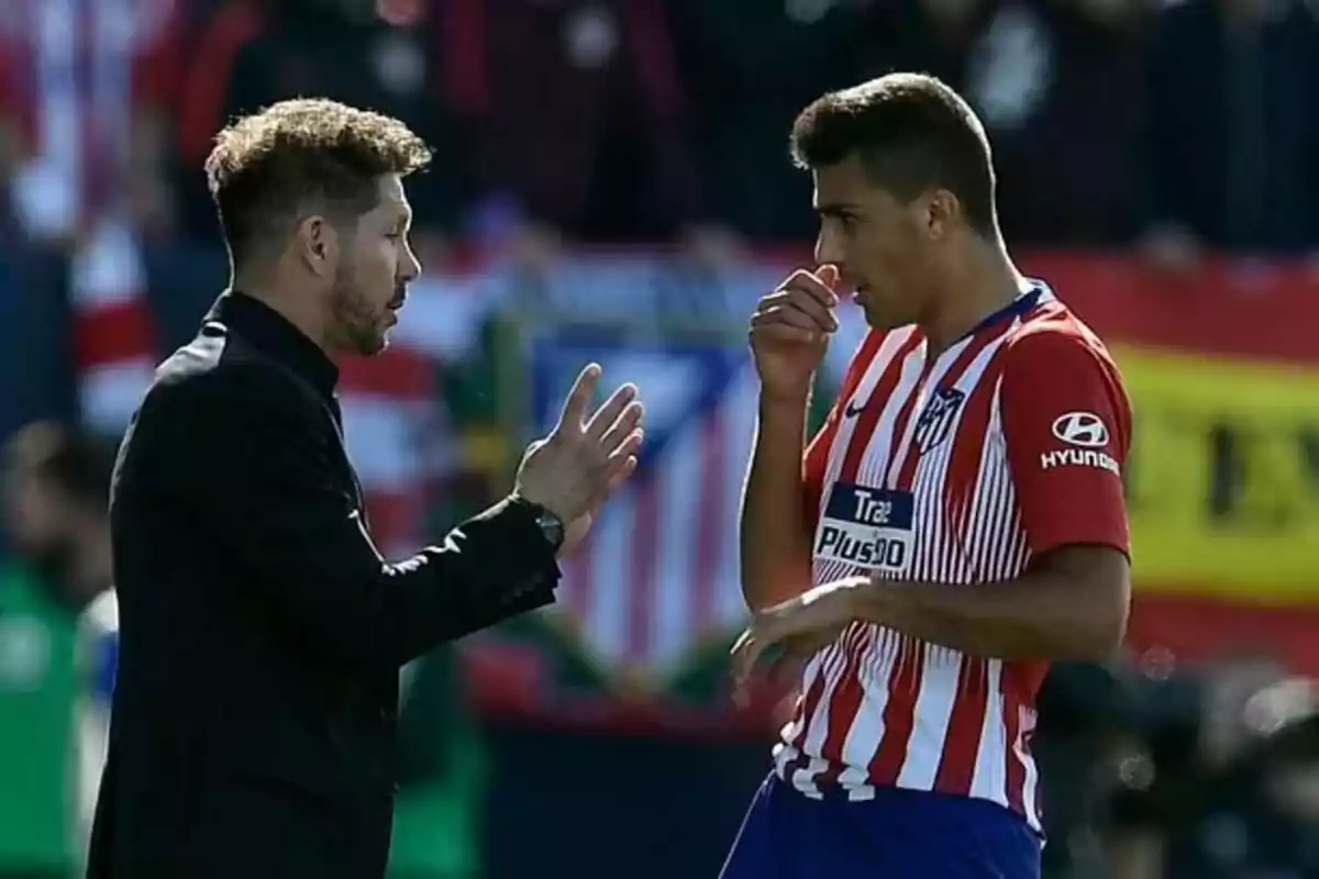 Un entrenador de fútbol hablando con un jugador del Atlético de Madrid en el campo.