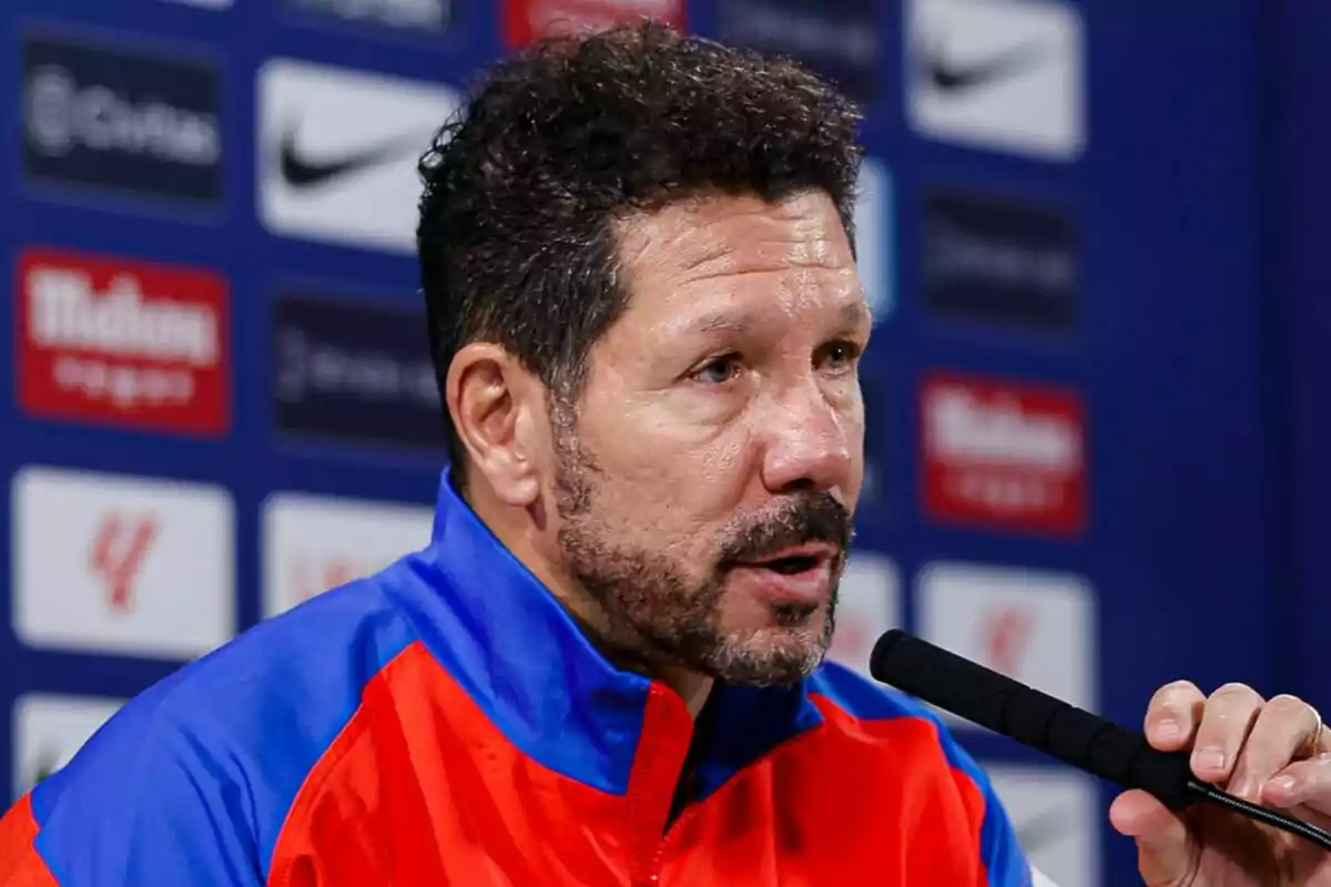 Un hombre con chaqueta azul y roja hablando en una conferencia de prensa.