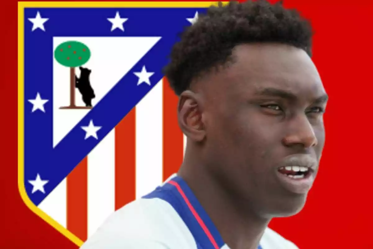 Jugador de fútbol con camiseta blanca frente al escudo del Atlético de Madrid sobre fondo rojo