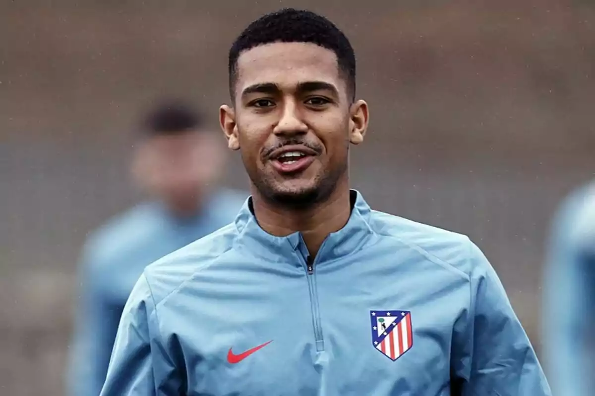 Un jugador de fútbol con una chaqueta de entrenamiento del Atlético de Madrid sonríe mientras está al aire libre.