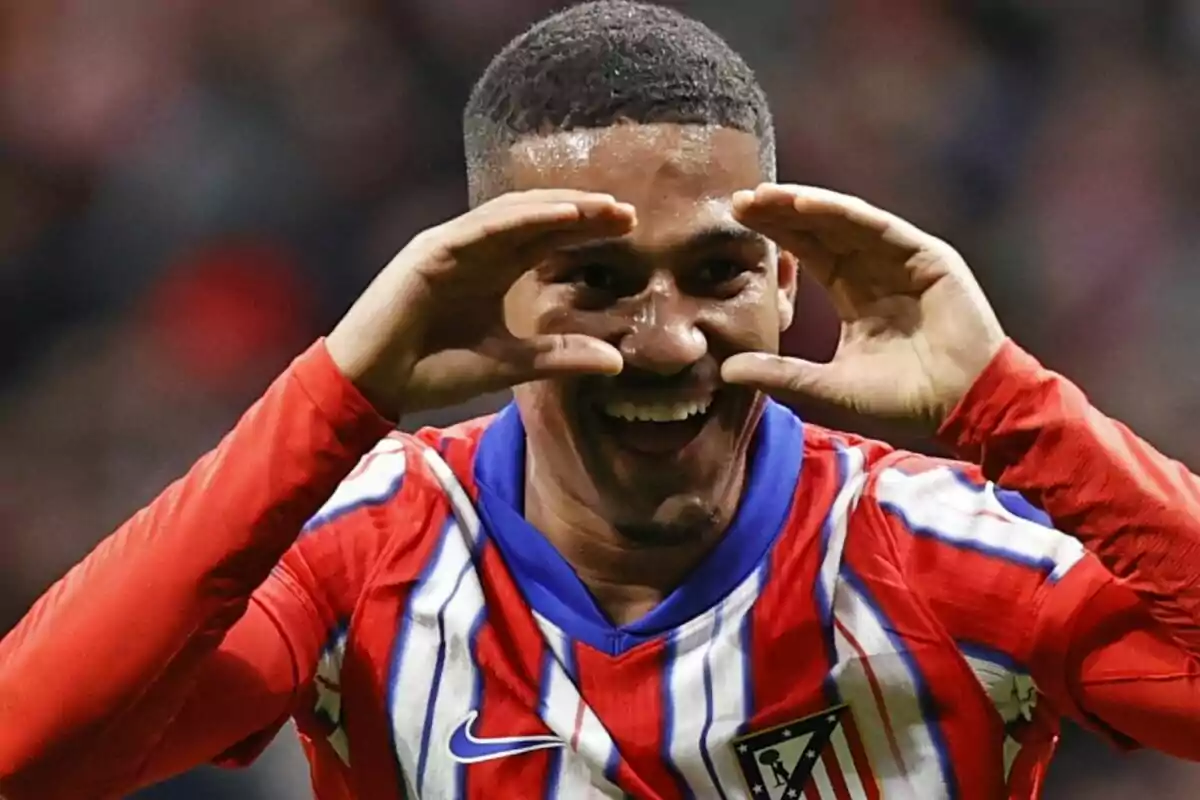 Un jugador de fútbol con la camiseta del Atlético de Madrid celebra un gol con una expresión alegre y las manos alrededor de los ojos.