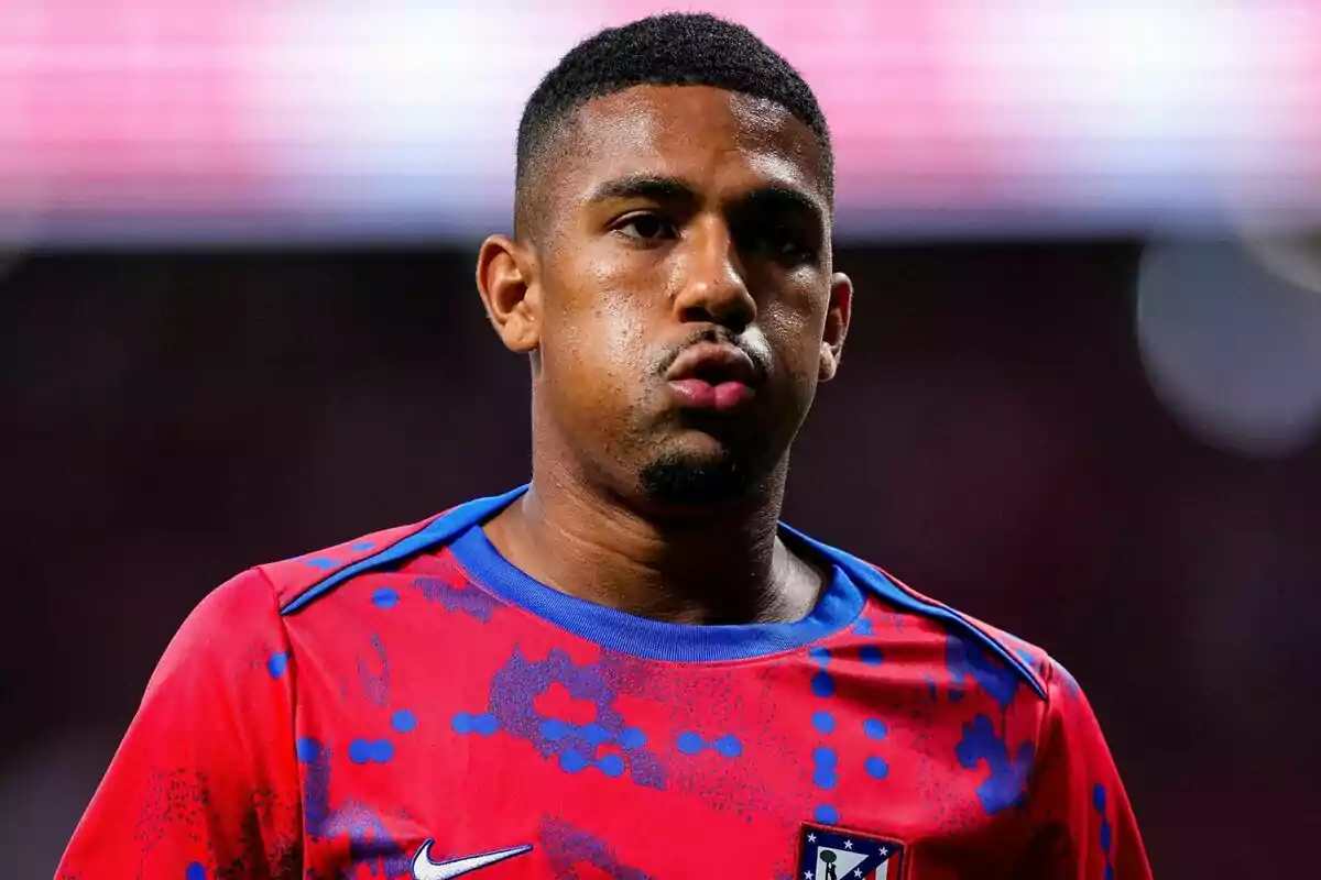 Jugador de fútbol con camiseta roja y azul del Atlético de Madrid en el campo.