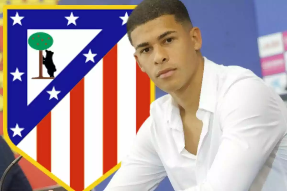 Un joven con camisa blanca está sentado frente a un escudo del Atlético de Madrid.