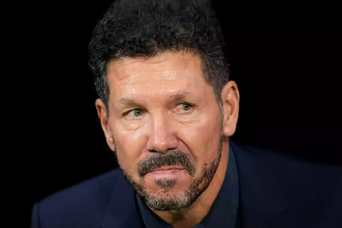 Hombre con barba y cabello rizado mirando hacia un lado con expresión seria.