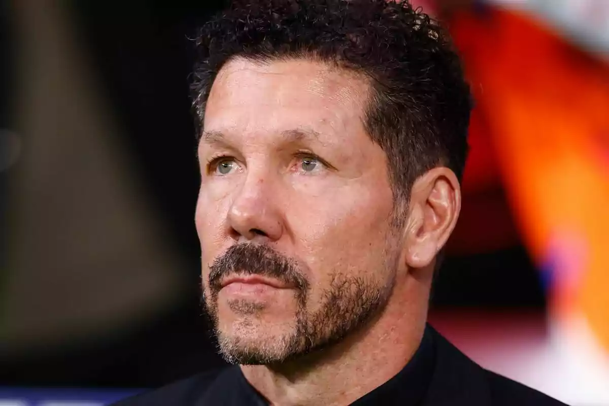 Un hombre con barba y cabello rizado mira hacia adelante con una expresión seria.