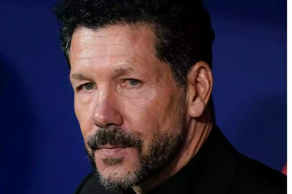 Un hombre con barba y cabello oscuro mira hacia un lado con expresión seria.