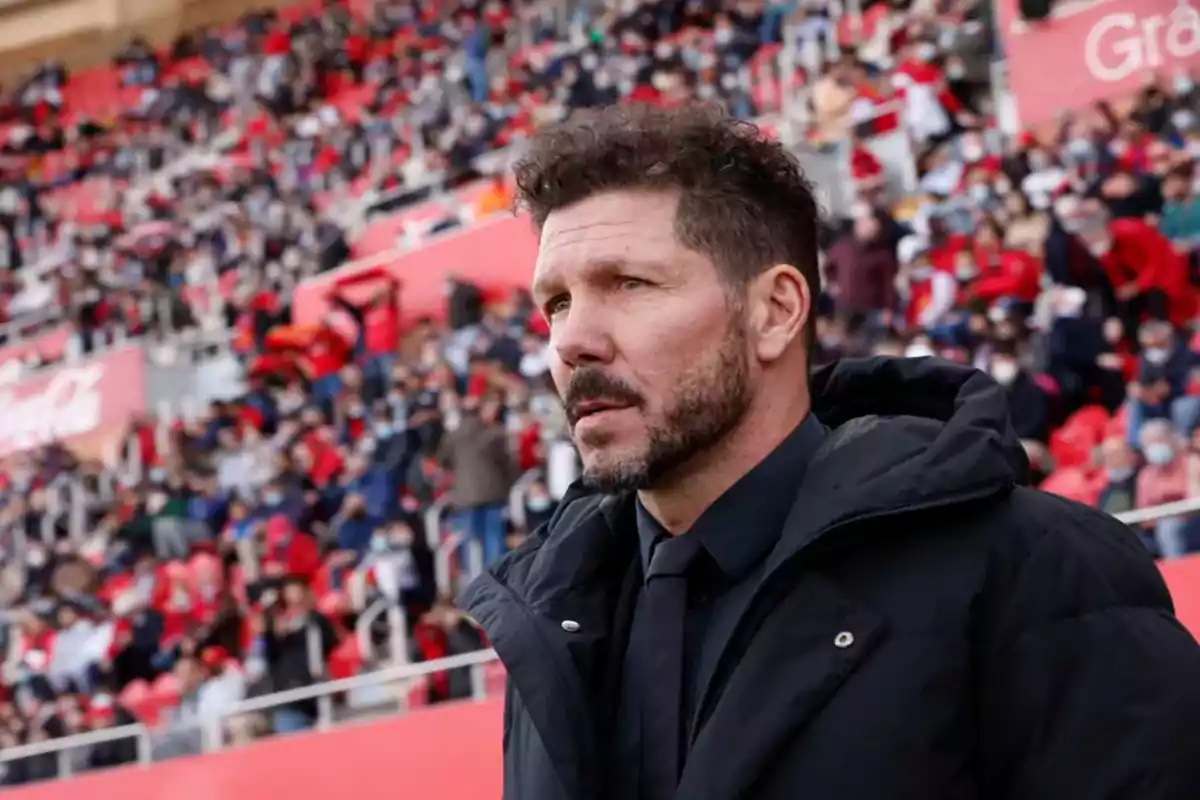 Un hombre con chaqueta negra en un estadio lleno de espectadores.