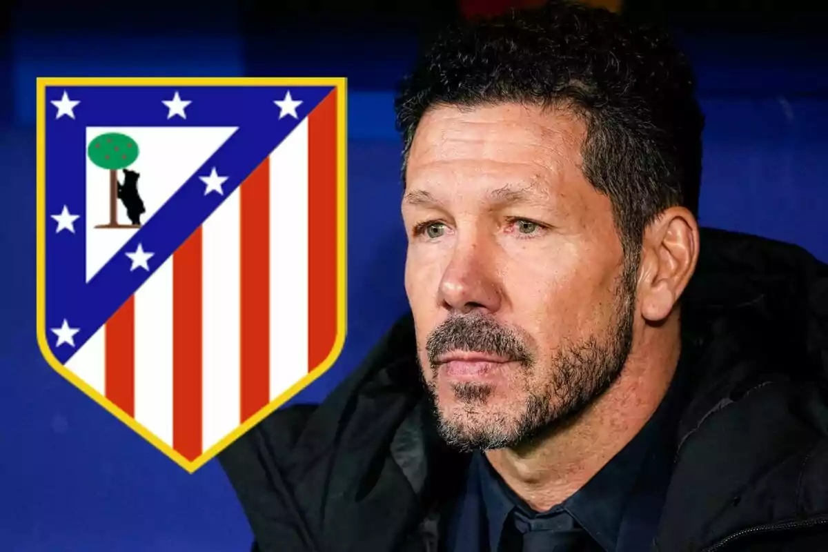 A man with a beard and dark hair is sitting, facing forward, next to the Atlético de Madrid crest.