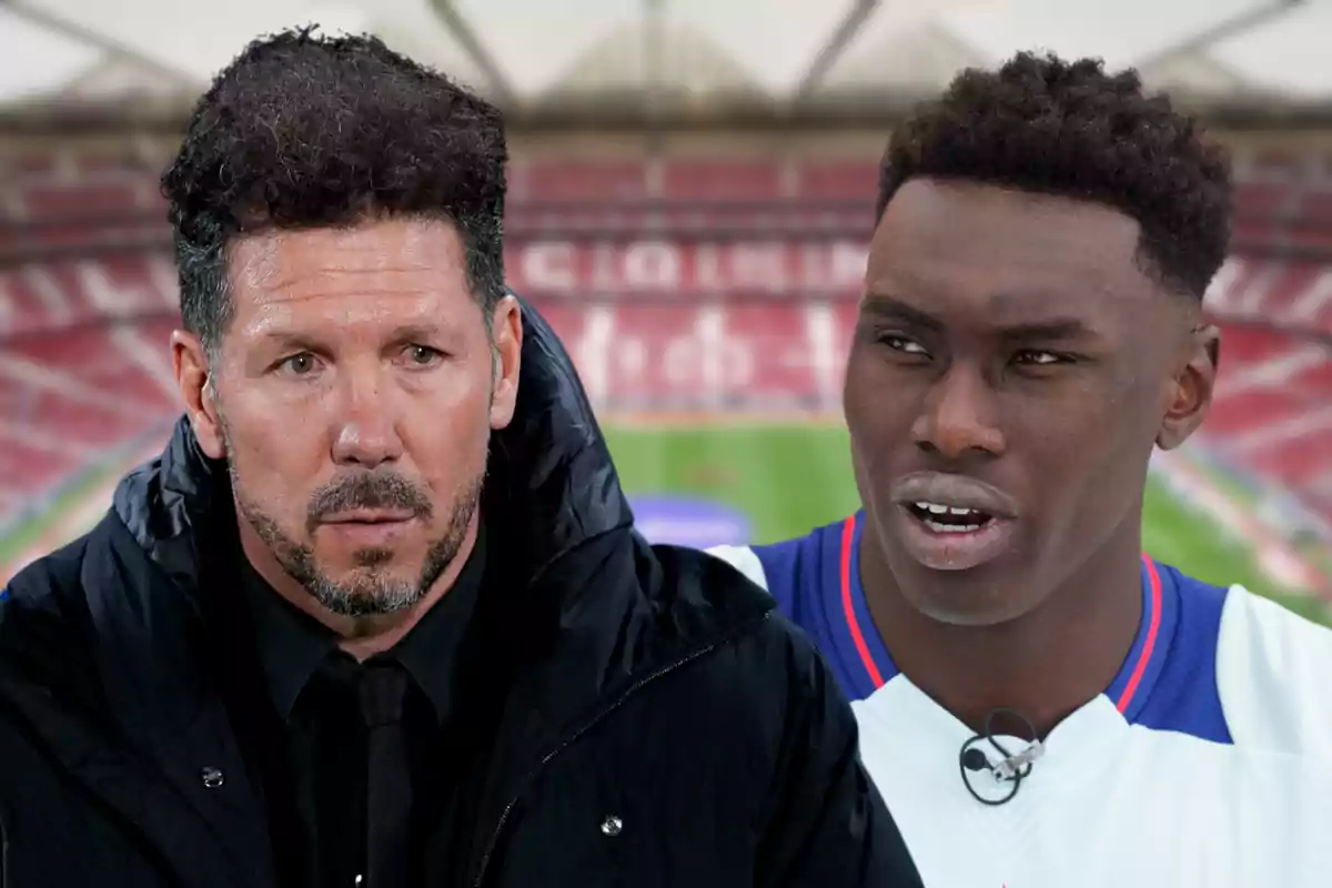 Dos hombres, uno con chaqueta negra y otro con camiseta blanca, están en un estadio de fútbol.