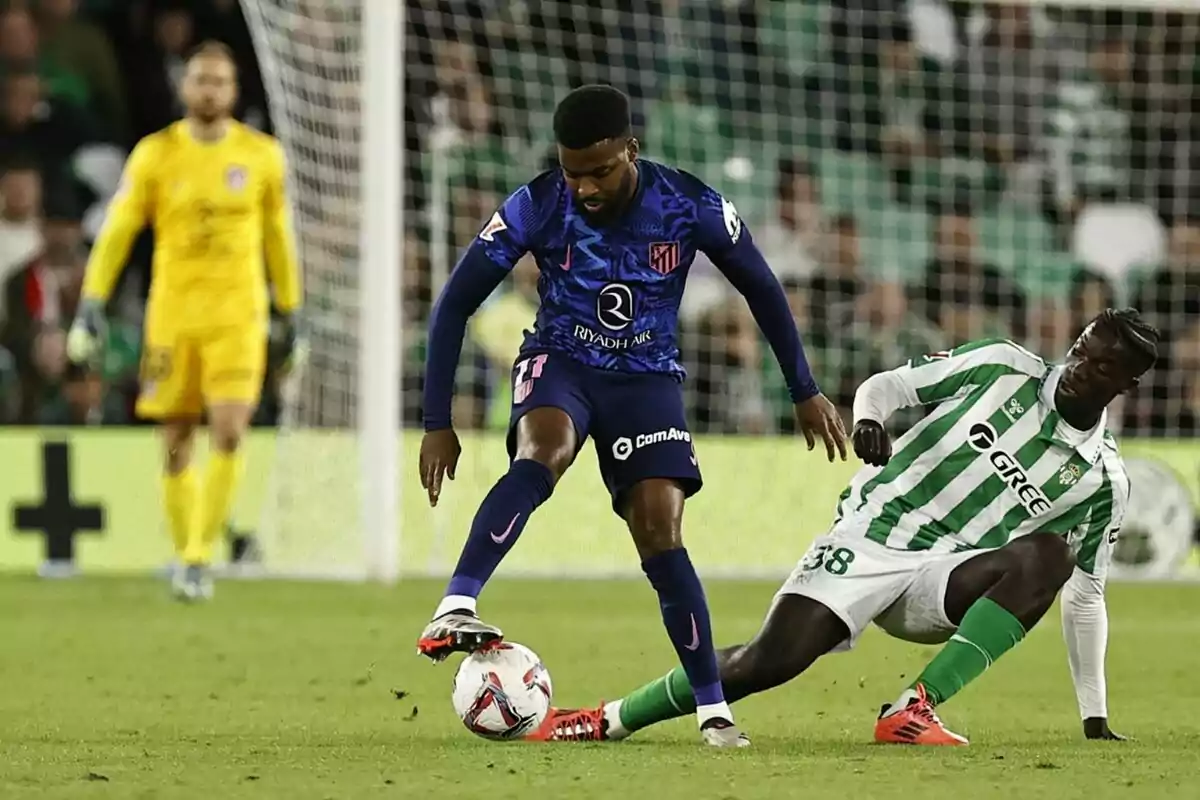 Un jugador del Atlético de Madrid disputa el balón con un jugador del Real Betis en un partido de fútbol.