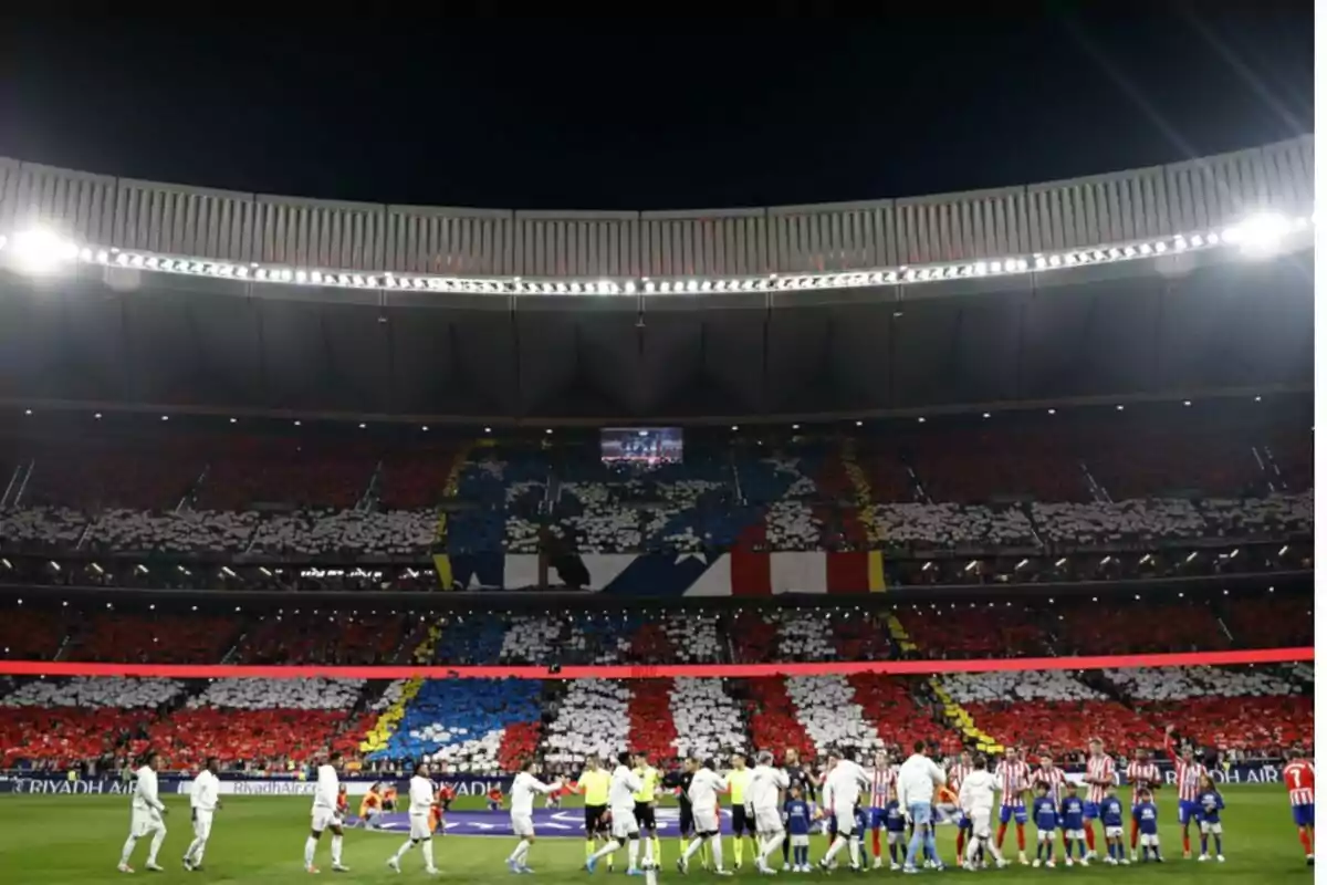 Jugadores de fútbol en el campo con una gran coreografía de colores en las gradas del estadio.