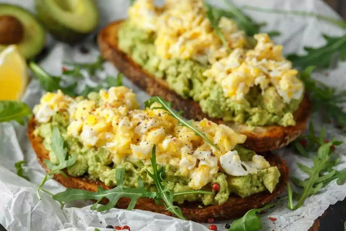 Dos tostadas con aguacate, huevo revuelto con queso y rúcula Dos tostadas con aguacate, huevo revuelto con queso y rúcula
