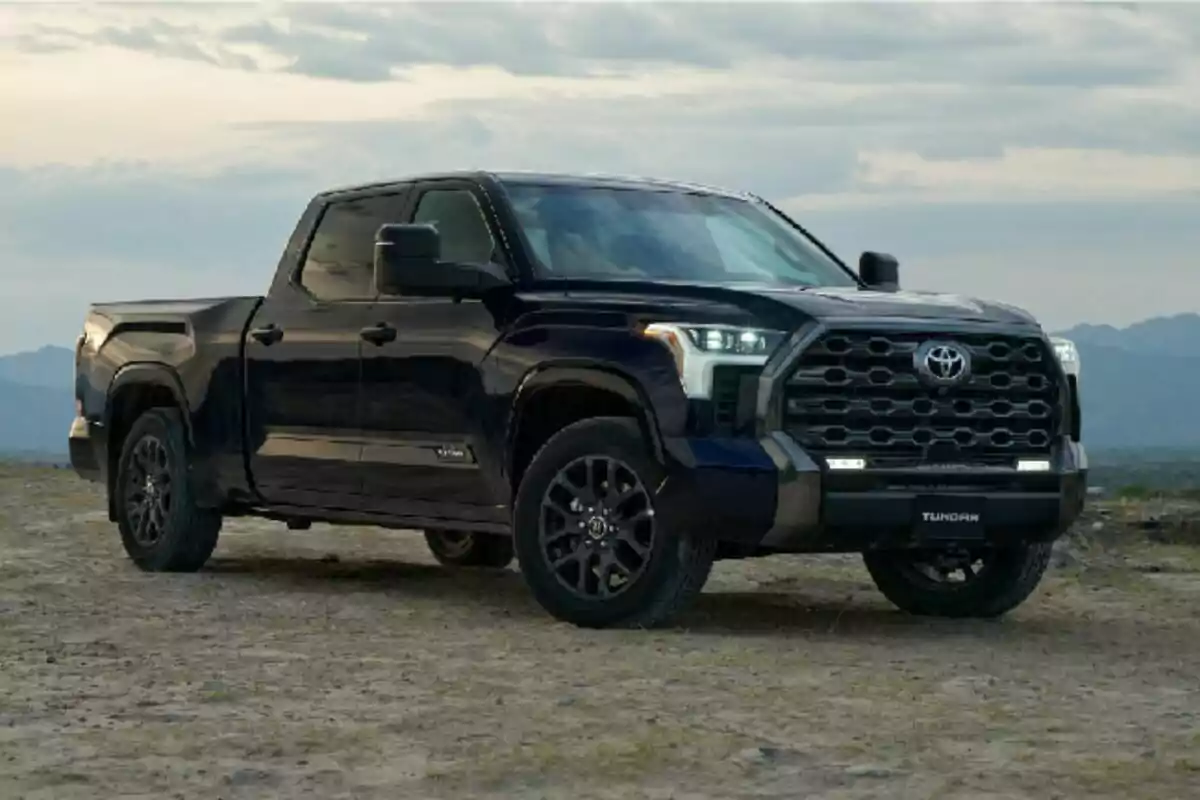 Camioneta pickup negra estacionada en un terreno al aire libre con montañas al fondo
