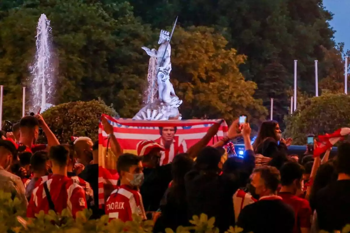 Fans celebrating with a flag in front of a fountain and a statue.