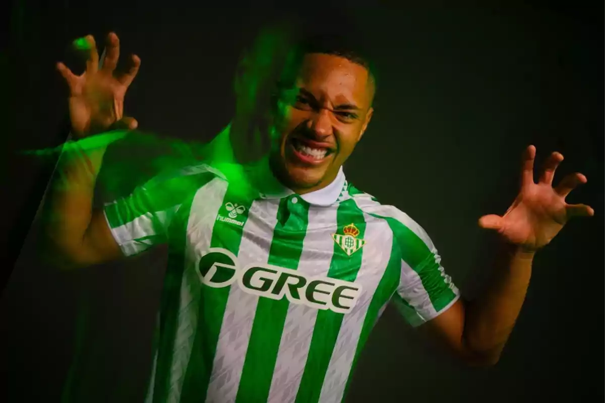 Un jugador de fútbol con la camiseta del Real Betis hace un gesto enérgico con las manos mientras sonríe.